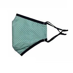 May include: A green face mask with white polka dots and black elastic ear loops.