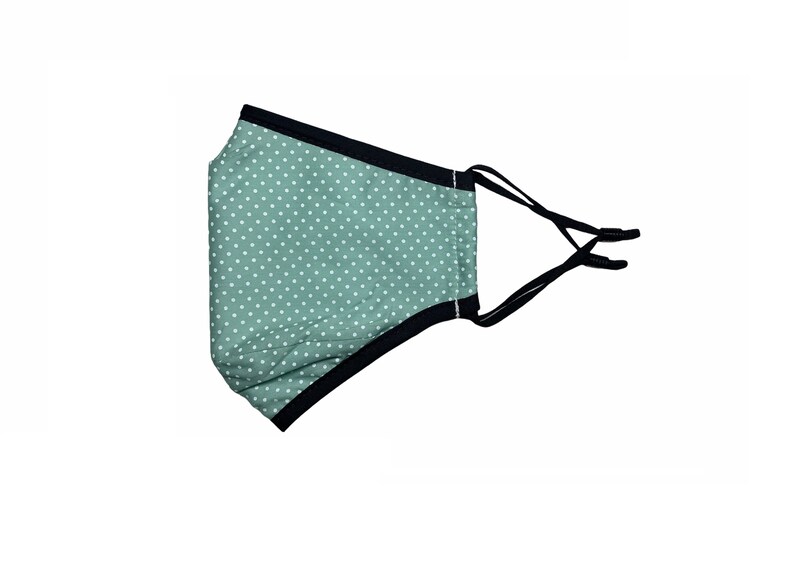 May include: A green face mask with white polka dots and black elastic ear loops.