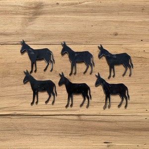 May include: Six black metal donkey silhouettes on a light brown wooden background.