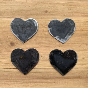 May include: Four black metal heart-shaped ornaments on a wooden background.
