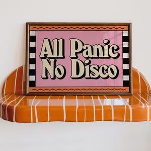 May include: A rectangular framed print with a pink background and the text All Panic No Disco in black letters. The frame features orange wavy lines at the top and bottom, with black and white vertical stripes on the sides, resting on an orange shelf.