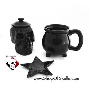 May include: A black ceramic skull-shaped jar with a lid, a black ceramic cauldron-shaped mug with three feet, and a black star-shaped dish. The image includes the text Shop of Skulls and the website address www.ShopOfSkulls.com.