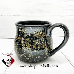 May include: Black ceramic mug with a speckled glaze in shades of white, yellow, and orange. The mug has a rounded body and a handle.