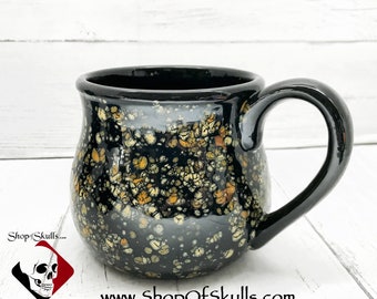 May include: Black ceramic mug with a speckled glaze in shades of white, yellow, and orange. The mug has a rounded body and a handle.