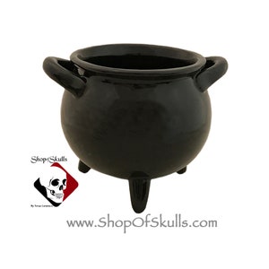 May include: A small black ceramic cauldron with three legs and two handles. The cauldron is a traditional Halloween decoration.