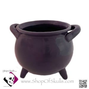 May include: A small purple ceramic cauldron with three legs and two handles. The cauldron is a decorative item and is perfect for Halloween or witchy decor.