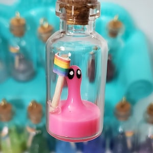 May include: A small glass bottle with a cork stopper contains a pink octopus with a rainbow flag. The bottle is hanging from a gold chain.