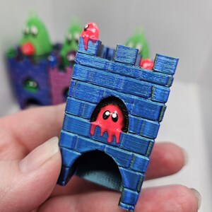 May include: A blue castle with a red ghost figure inside and a red ghost figure on top. The castle is made of 3D printed plastic.