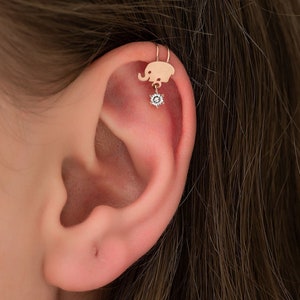 May include: A gold-toned elephant ear cuff with a small, clear gemstone dangling from the bottom.
