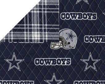 May include: Reversible fabric featuring a navy blue side with white stars, the word "COWBOYS", and a football helmet. The reverse side has a white and gray plaid pattern. The fabric is quilted with white stitching.