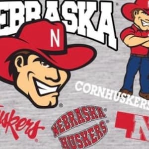May include: A gray background features multiple Nebraska Cornhuskers logos and graphics. The primary graphic is a smiling cartoon man wearing a red cowboy hat with a white "N". Other graphics include the word "Nebraska" and the word "Cornhuskers".