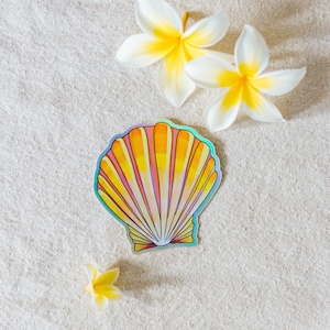 May include: A yellow and pink seashell sticker with a holographic finish on a white fabric background. There are three white flowers with yellow centers on the fabric.