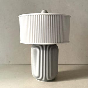 May include: A white table lamp with a fluted ceramic base and a white fabric shade with vertical pleats.