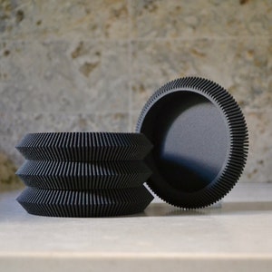 May include: Three black, round, decorative trays with a ridged, textured edge. The trays are stacked on top of each other.
