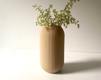 Puede incluir: Un jarrón de cerámica de color marrón claro, con nervaduras, con un pequeño ramo de flores blancas.