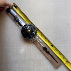 May include: Black clock hands with a gold accent on a wooden base. The hands are packaged with a clear plastic wrap and a yellow measuring tape.