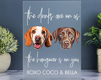 Op de afbeelding: Een lichtblauw acryl bord met de tekst "The drinks are on us, the hangover is on you, XOXO Coco & Bella". Twee hondenportretten zijn afgebeeld op het bord, een bruin-wit en de andere bruin.