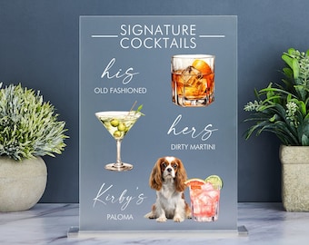 May include: A clear acrylic sign with the text "Signature Cocktails" at the top. The sign features three cocktails: "his" Old Fashioned, "hers" Dirty Martini, and "Kirby's" Paloma. Each cocktail is illustrated with a watercolour image. A dog is sitting below the cocktails.