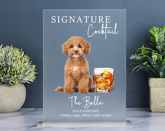 Op de afbeelding: Een helder glazen bord met de tekst "SIGNATURE Cocktail The Bella OLD FASHIONED whiskey, sugar, bitters, water, orange" en een afbeelding van een kleine bruine hond en een glas sinaasappelsap.