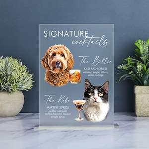 May include: A clear acrylic sign with the text "SIGNATURE cocktails" at the top. The sign features two cocktails, "The Billie" and "The Kobe", with illustrations of a dog and a cat. The Billie is an Old Fashioned, and The Kobe is a Martini Express.