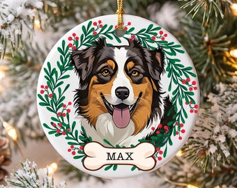 May include: A round white ceramic ornament featuring a colorful illustration of an Australian Shepherd dog with a black, white, and tan coat. The dog is framed by a green holly wreath with red berries and a bone-shaped tag labeled with the name MAX.
