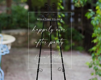 Peut inclure: Chevalet en métal noir avec un panneau en acrylique transparent. Le panneau indique "WELCOME TO OUR happily ever after party" avec les noms Lauren & Jackson et la date du 25 avril 2025, à San Diego, CA.