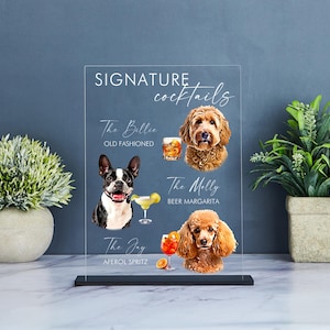 May include: Clear acrylic sign with the text "Signature Cocktails" at the top.  The sign features three cocktails with dog illustrations and names: "The Billie Old Fashioned", "The Molly Beer Margarita", and "The Jay Aperol Spritz".