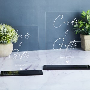 May include: Two clear acrylic signs with black bases, each with the text "Cards & Gifts" and "Thank You!" in white cursive writing.