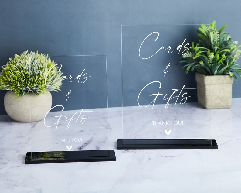 May include: Two clear acrylic signs with black bases, each with the text "Cards & Gifts" and "Thank You!" in white cursive writing.
