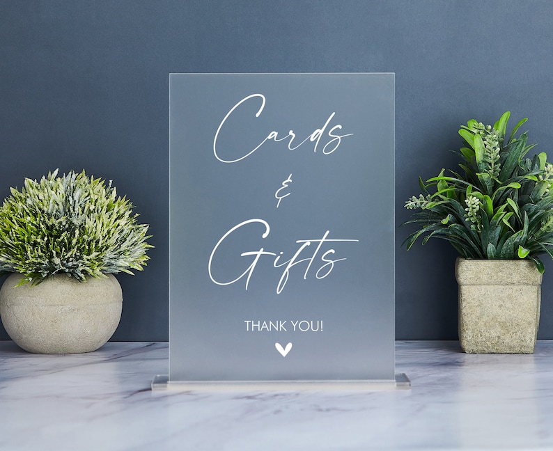 May include: A clear acrylic sign with the text "Cards & Gifts" in white script font. The sign also includes the text "Thank You!" and a small heart.