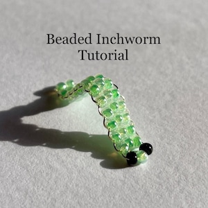 以下が含まれることがあります： 緑色の虹色のビーズと黒いビーズでできたビーズのイモムシ。イモムシはCの形に曲がっています。画像には「ビーズのイモムシのチュートリアル」というテキストが含まれています。