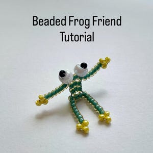 May include: A beaded frog figure with green body, yellow feet and hands, and large white eyes with black pupils. The text "Beaded Frog Friend Tutorial" is above the frog.