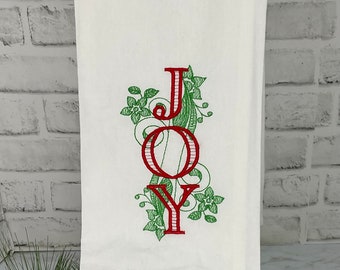 Puede incluir: Toalla de cocina blanca con bordado rojo y verde de la palabra "JOY" con adornos decorativos.