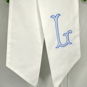 May include: White fabric table runner with a blue embroidered letter L.