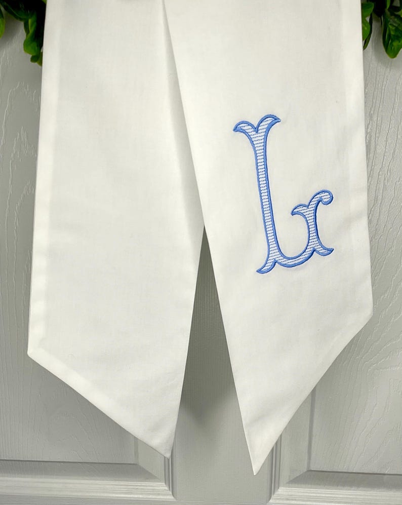 May include: White fabric table runner with a blue embroidered letter L.