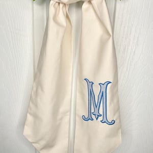 May include: A white fabric door swag with a blue and white monogram of the letter "M" embroidered on it.