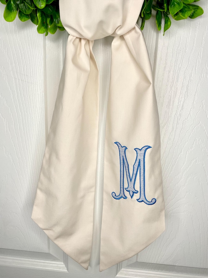 May include: A white fabric door swag with a blue and white monogram of the letter "M" embroidered on it.