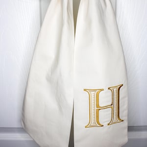 May include: A white fabric door swag with a gold embroidered letter "H" on it.