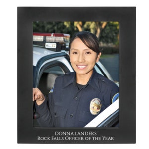 May include: A black picture frame with a photo of a woman in a police uniform standing next to a police car. The text "DONNA LANDERS ROCK FALLS OFFICER OF THE YEAR" is printed below the photo.