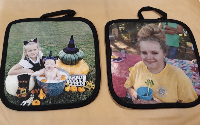 Puede incluir: Dos agarraderas de olla de tela negra y blanca con im&aacute;genes impresas en ellas. La primera agarradera tiene una foto de dos ni&ntilde;as peque&ntilde;as vestidas con disfraces de Halloween. La segunda agarradera tiene una foto de una joven sonriendo y sosteniendo una taza azul con una pajita.