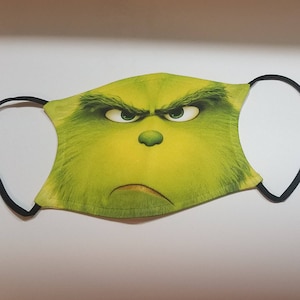 May include: Green face mask with a printed image of the Grinch from the movie How the Grinch Stole Christmas. The Grinch is frowning with his eyebrows furrowed and his eyes wide open.