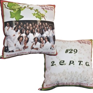 Op de afbeelding: Twee decoratieve kussens met een witte achtergrond. Het eerste kussen heeft een groepsfoto van vrouwen in witte gewaden met de tekst "Alpha Kappa Alpha Sorority, Inc." en "Made In 2005 by Beta Psi". Het tweede kussen heeft een witte achtergrond met witte stippen en de tekst "#29 2. C. P. T. G. Alpha Kappa Alpha Sorority, Inc." en "Made In 2009 by Beta Psi".