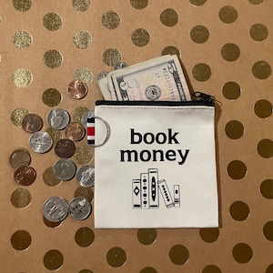 May include: White canvas coin purse with a black zipper and the text "book money" printed in black. The purse is open and filled with US currency and coins.