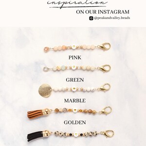 May include: Five beaded lanyards in pink, green, marble, golden, and leopard patterns. Each lanyard features a gold clasp and small heart-shaped beads. The text "FINDE MORE PHOTO inspiration ON OUR INSTAGRAM @peakandvalley.beads" is at the top.