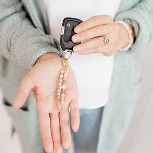 May include: A car key fob with a decorative beaded keychain. The keychain features a mix of pastel-colored beads and gold accents. The key fob is black with silver buttons.