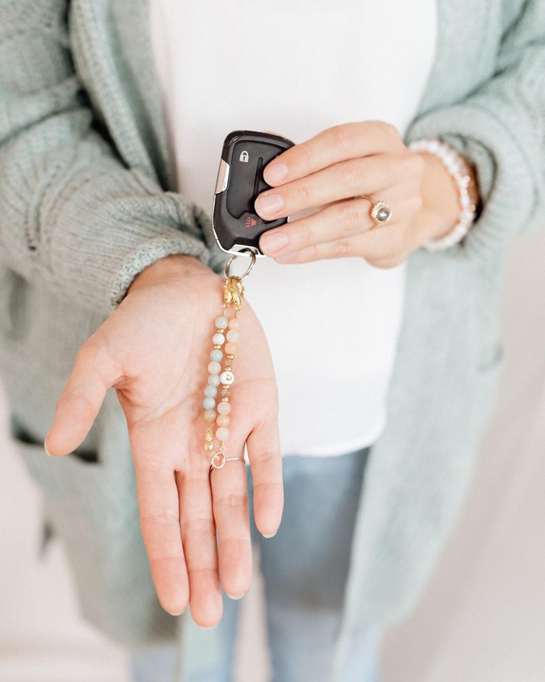May include: A car key fob with a decorative beaded keychain. The keychain features a mix of pastel-colored beads and gold accents. The key fob is black with silver buttons.