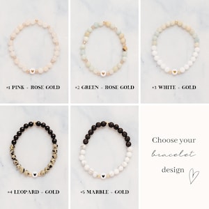 May include: Five different beaded bracelets are displayed, each with a unique design. The bracelets include pink, green, white, leopard, and marble beads, paired with gold accents. Each bracelet has a small heart charm. Text reads: "Choose your bracelet design."