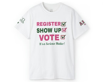 May include: A white short-sleeved t-shirt featuring the text REGISTER, SHOW UP, and VOTE in pink and green with checkmark boxes. Below the text is the phrase It's a Serious Matter! in green. The sleeves feature green and pink Greek letter graphics.