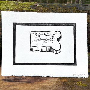 May include: Black and white illustration of a bug lying on a piece of toast. The illustration is framed in a black border and signed "INKMAMMAL" in the bottom right corner.