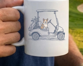 May include: White ceramic mug featuring a cartoon illustration of a corgi dog driving a golf cart. The golf cart is light blue and has golf clubs in the back. The mug has a white handle and is held by a person.